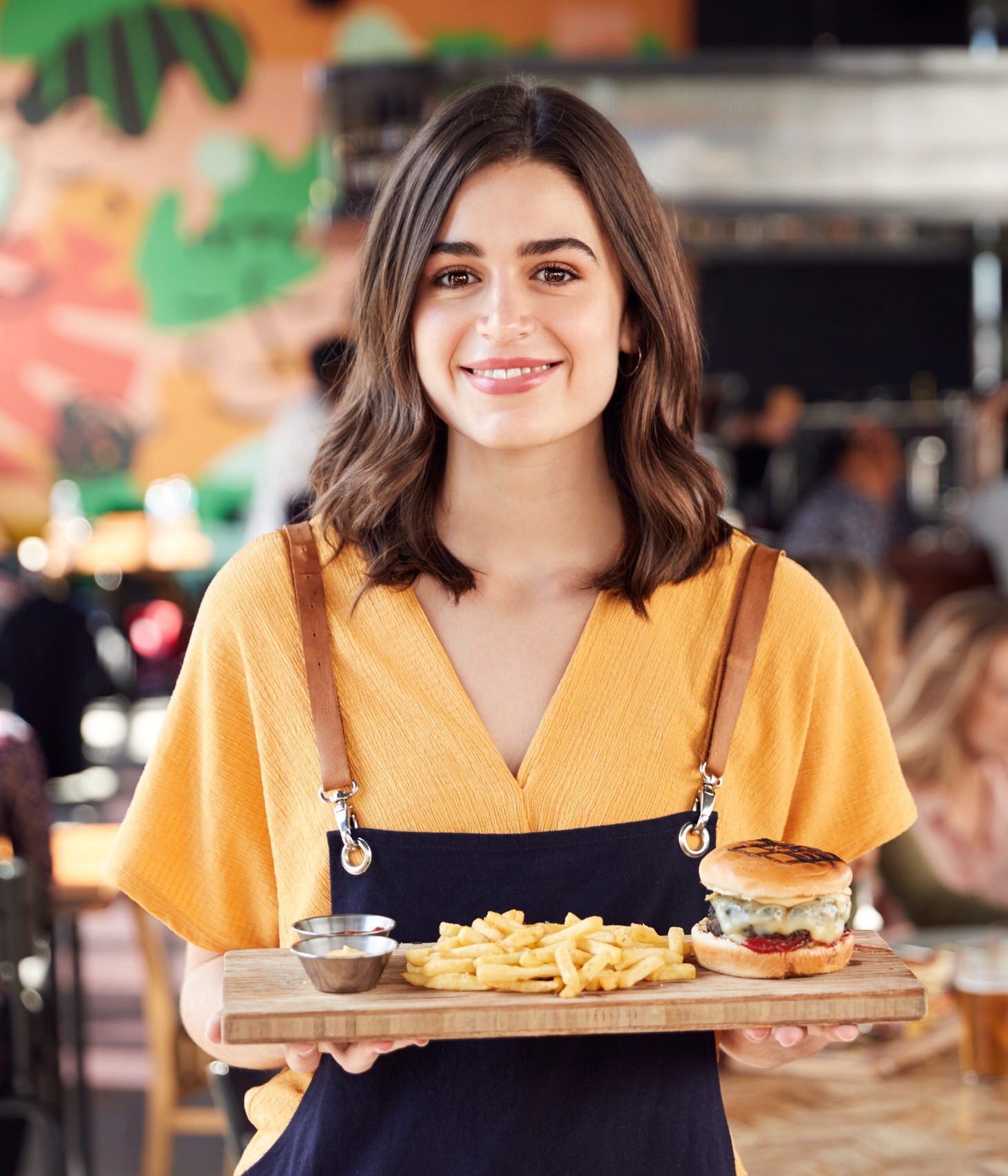 Se lancer dans la restauration : serveuse souriante portant un plateau dans un restaurant animé, accompagnée par Normizy pour le dossier ERP