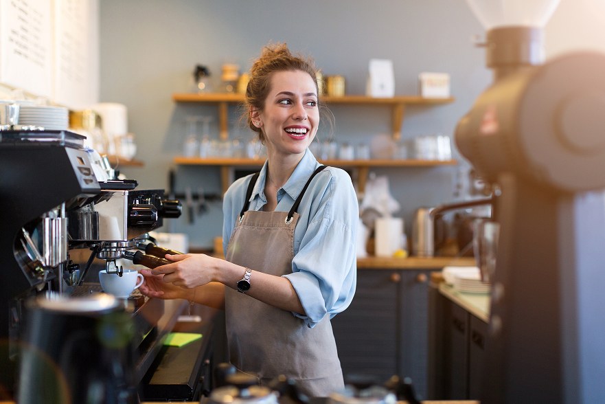 Barista souriante en tablier préparant un expresso au percolateur derrière le comptoir d'un bar