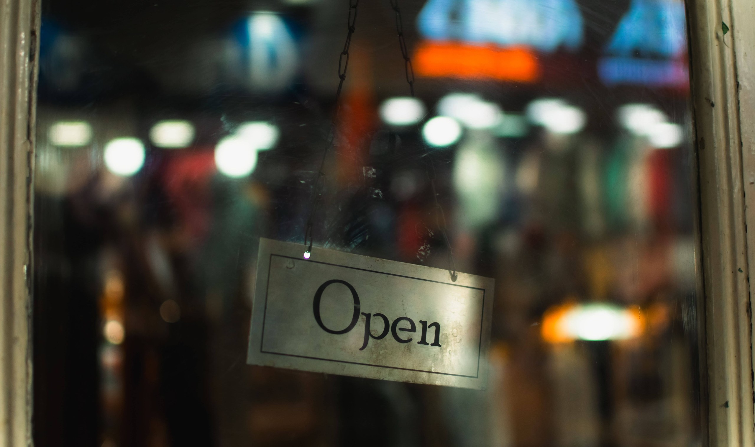 Panneau Open suspendu derrière la vitrine d'une boutique, avec l'intérieur éclairé et flou en arrière-plan